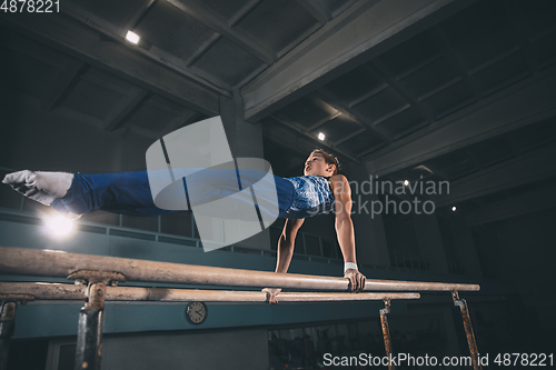 Image of Little male gymnast training in gym, flexible and active. Caucasian fit little boy, athlete in sportswear practicing in exercises for strength, balance.