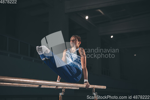 Image of Little male gymnast training in gym, flexible and active. Caucasian fit little boy, athlete in sportswear practicing in exercises for strength, balance.