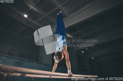 Image of Little male gymnast training in gym, flexible and active. Caucasian fit little boy, athlete in sportswear practicing in exercises for strength, balance.