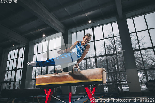 Image of Little male gymnast training in gym, flexible and active. Caucasian fit little boy, athlete in sportswear practicing in exercises for strength, balance.