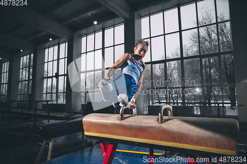 Image of Little male gymnast training in gym, flexible and active. Caucasian fit little boy, athlete in sportswear practicing in exercises for strength, balance.