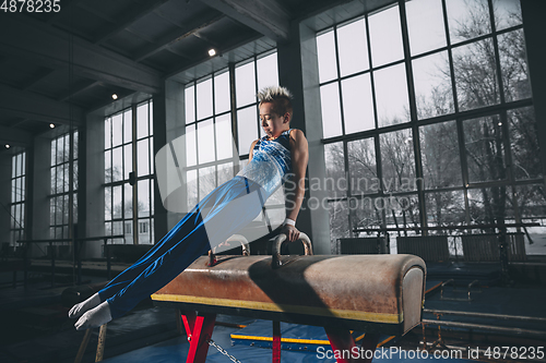 Image of Little male gymnast training in gym, flexible and active. Caucasian fit little boy, athlete in sportswear practicing in exercises for strength, balance.