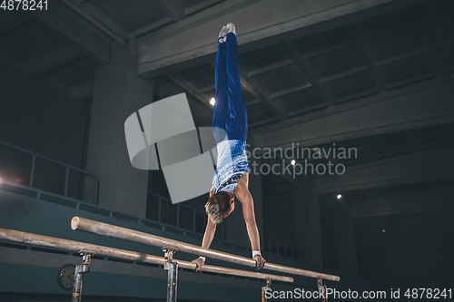 Image of Little male gymnast training in gym, flexible and active. Caucasian fit little boy, athlete in sportswear practicing in exercises for strength, balance.