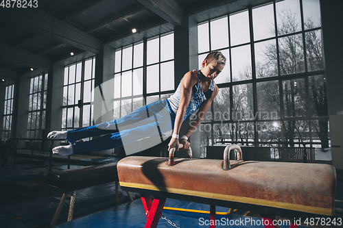 Image of Little male gymnast training in gym, flexible and active. Caucasian fit little boy, athlete in sportswear practicing in exercises for strength, balance.