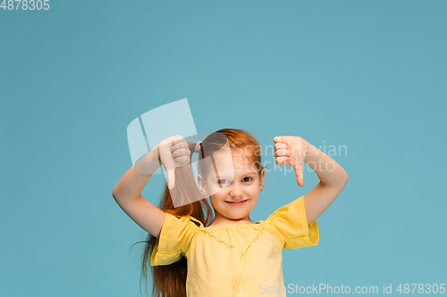 Image of Happy caucasian little girl isolated on blue studio background. Looks happy, cheerful, sincere. Copyspace. Childhood, education, emotions concept