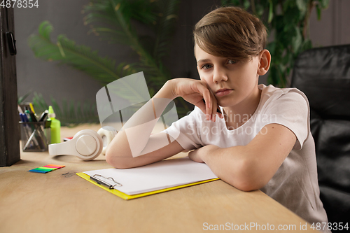 Image of Little boy sitting at the table during listening to teacher on online videocall, educational course