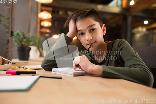 Image of Little boy sitting at the table during listening to teacher on online videocall, educational course