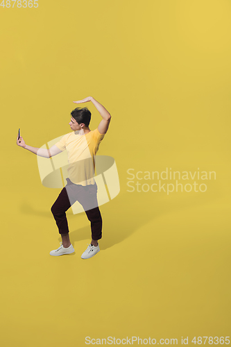 Image of High angle view of young man on yellow studio background. Boy in motion, jumping high. Human emotions and facial expressions concept