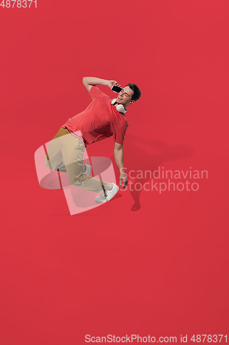 Image of High angle view of young man on red studio background. Boy in motion, jumping high. Human emotions and facial expressions concept