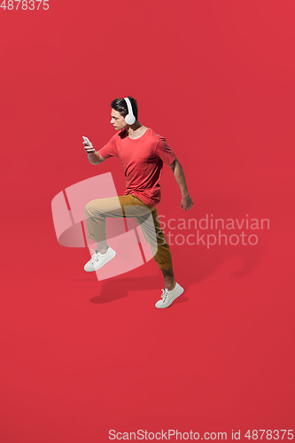 Image of High angle view of young man on red studio background. Boy in motion, jumping high. Human emotions and facial expressions concept