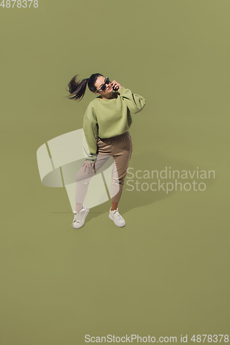 Image of High angle view of young woman on green studio background. Girl in motion or movement. Human emotions and facial expressions concept