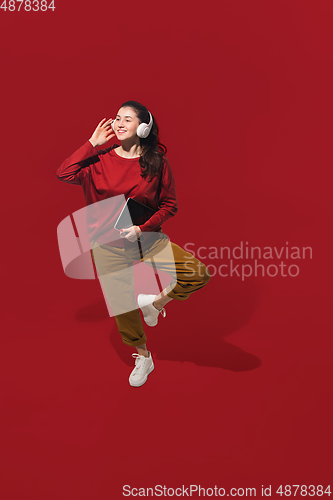 Image of High angle view of young woman on red studio background. Girl in motion or movement. Human emotions and facial expressions concept