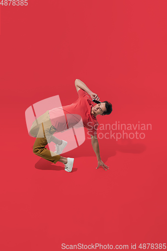 Image of High angle view of young man on red studio background. Boy in motion, jumping high. Human emotions and facial expressions concept