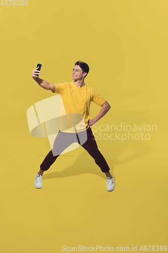 Image of High angle view of young man on yellow studio background. Boy in motion, jumping high. Human emotions and facial expressions concept