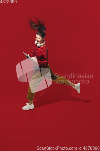 Image of High angle view of young woman on red studio background. Girl in motion or movement. Human emotions and facial expressions concept