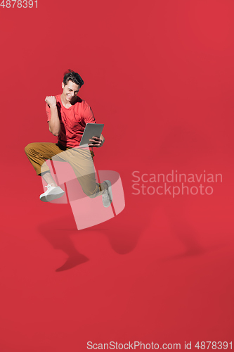 Image of High angle view of young man on red studio background. Boy in motion, jumping high. Human emotions and facial expressions concept