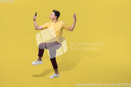 Image of High angle view of young man on yellow studio background. Boy in motion, jumping high. Human emotions and facial expressions concept