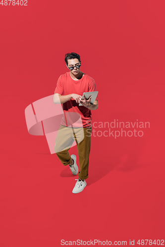 Image of High angle view of young man on red studio background. Boy in motion, jumping high. Human emotions and facial expressions concept