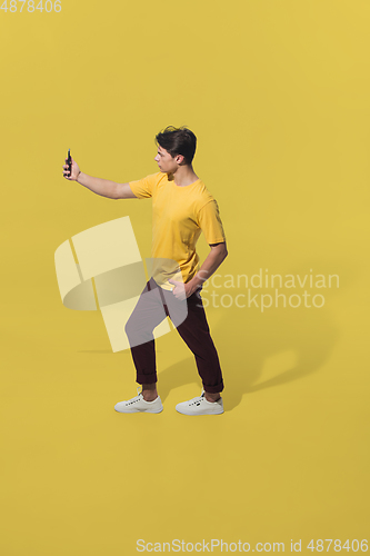 Image of High angle view of young man on yellow studio background. Boy in motion, jumping high. Human emotions and facial expressions concept