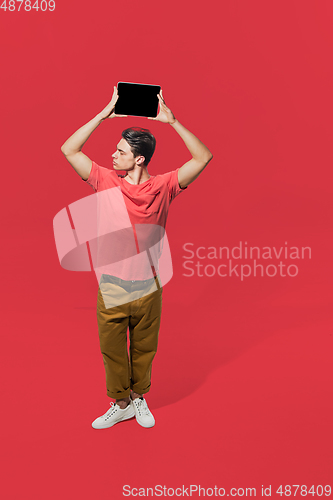 Image of High angle view of young man on red studio background. Boy in motion, jumping high. Human emotions and facial expressions concept