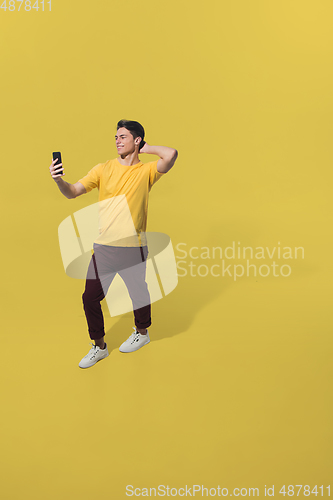 Image of High angle view of young man on yellow studio background. Boy in motion, jumping high. Human emotions and facial expressions concept