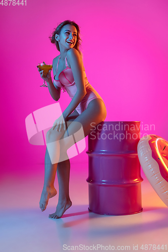 Image of Beautiful girl in fashionable swimsuit isolated on gradient studio background in neon light. Summer, resort, fashion and weekend concept