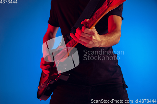 Image of Young caucasian musician playing guitar in neon light on blue background, inspired