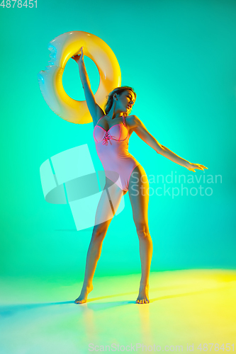 Image of Beautiful girl in fashionable swimsuit isolated on gradient studio background in neon light. Summer, resort, fashion and weekend concept