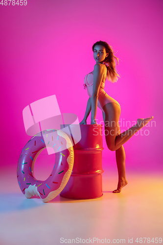 Image of Beautiful girl in fashionable swimsuit isolated on gradient studio background in neon light. Summer, resort, fashion and weekend concept