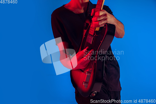 Image of Young caucasian musician playing guitar in neon light on blue background, inspired