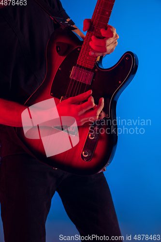 Image of Young caucasian musician playing guitar in neon light on blue background, inspired