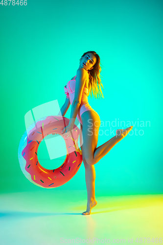 Image of Beautiful girl in fashionable swimsuit isolated on gradient studio background in neon light. Summer, resort, fashion and weekend concept