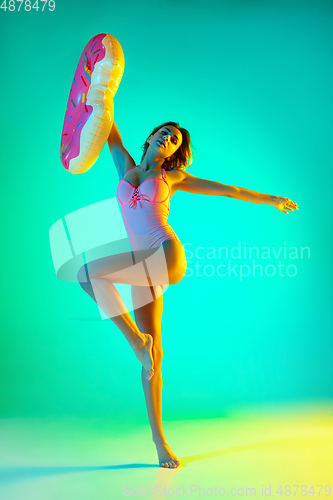 Image of Beautiful girl in fashionable swimsuit isolated on gradient studio background in neon light. Summer, resort, fashion and weekend concept
