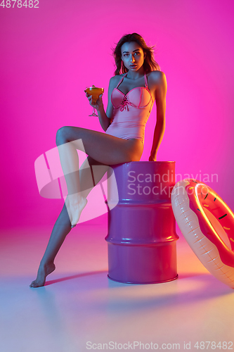 Image of Beautiful girl in fashionable swimsuit isolated on gradient studio background in neon light. Summer, resort, fashion and weekend concept