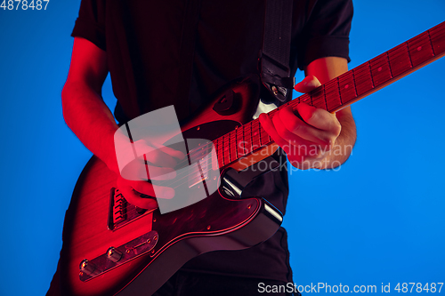 Image of Young caucasian musician playing guitar in neon light on blue background, inspired