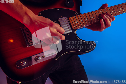 Image of Young caucasian musician playing guitar in neon light on blue background, inspired