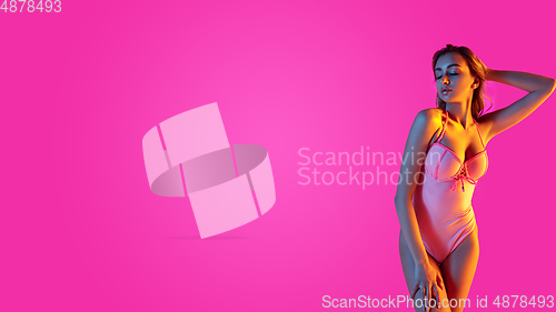 Image of Beautiful girl in fashionable swimsuit isolated on gradient studio background in neon light. Summer, resort, fashion and weekend concept