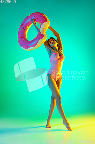 Image of Beautiful girl in fashionable swimsuit isolated on gradient studio background in neon light. Summer, resort, fashion and weekend concept