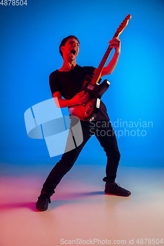 Image of Young caucasian musician playing guitar in neon light on blue background, inspired