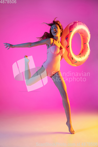 Image of Beautiful girl in fashionable swimsuit isolated on gradient studio background in neon light. Summer, resort, fashion and weekend concept