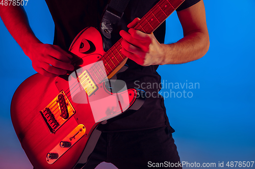Image of Young caucasian musician playing guitar in neon light on blue background, inspired
