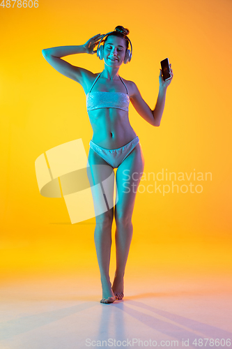 Image of Fashion portrait of seductive girl in stylish swimwear posing on a bright yellow background. Summertime, beach season