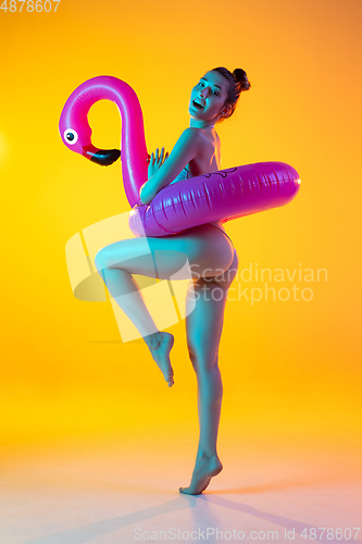 Image of Fashion portrait of seductive girl in stylish swimwear posing on a bright yellow background. Summertime, beach season