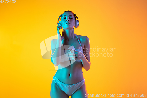 Image of Fashion portrait of seductive girl in stylish swimwear posing on a bright yellow background. Summertime, beach season