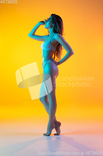 Image of Fashion portrait of seductive girl in stylish swimwear posing on a bright yellow background. Summertime, beach season