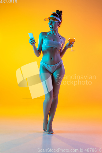 Image of Fashion portrait of seductive girl in stylish swimwear posing on a bright yellow background. Summertime, beach season