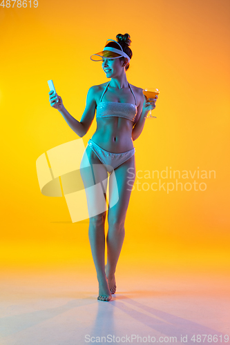 Image of Fashion portrait of seductive girl in stylish swimwear posing on a bright yellow background. Summertime, beach season