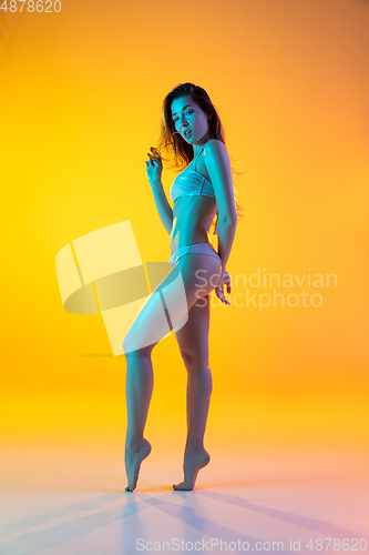Image of Fashion portrait of seductive girl in stylish swimwear posing on a bright yellow background. Summertime, beach season