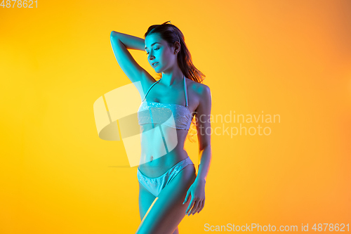 Image of Fashion portrait of seductive girl in stylish swimwear posing on a bright yellow background. Summertime, beach season