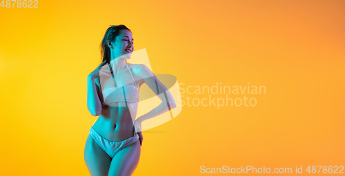 Image of Fashion portrait of seductive girl in stylish swimwear posing on a bright yellow background. Summertime, beach season